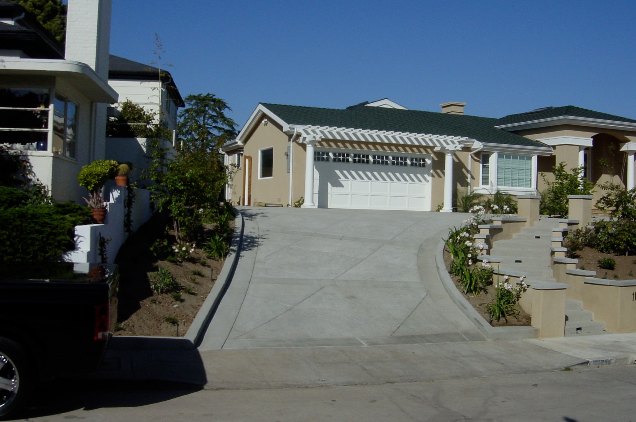 Smooth concrete driveway with diagonal score lines and clean flatwork at white home with pergola in San Fernando Valley, CA by Concrete Etc., Inc.