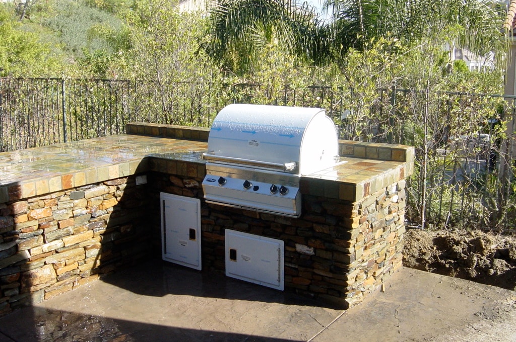 Custom outdoor kitchen with stacked stone veneer, built-in BBQ grill and stainless steel doors on concrete patio in Los Angeles by Concrete Etc., Inc.