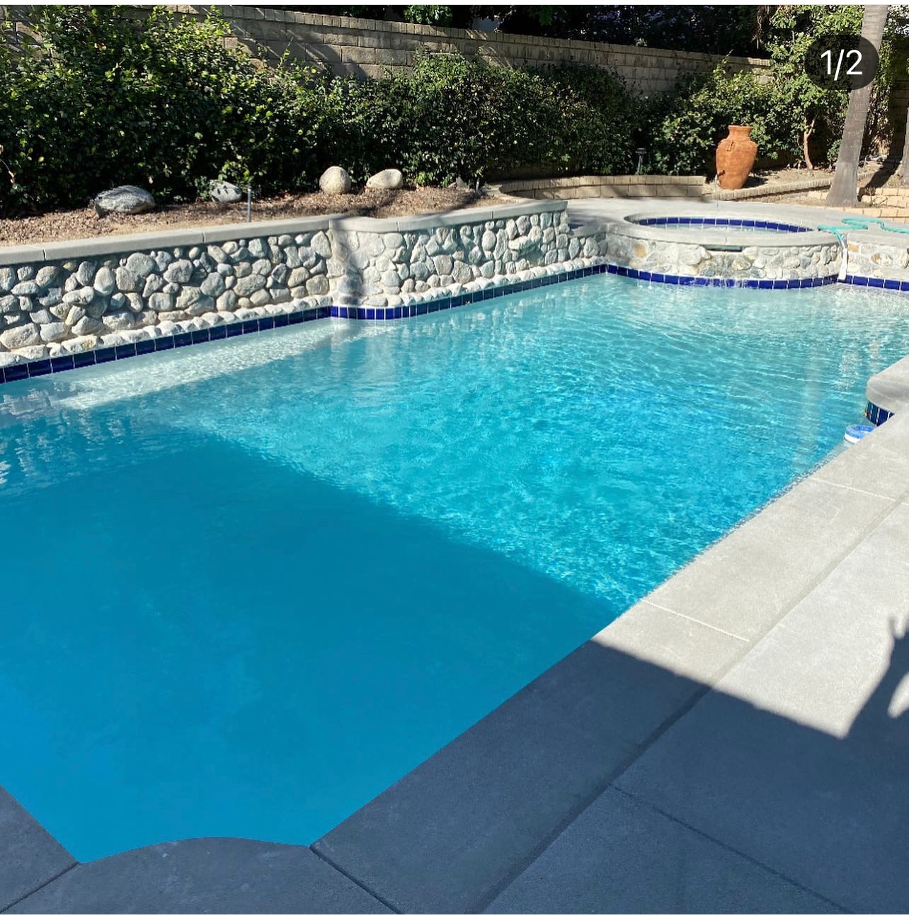 Sand finish concrete pool deck with coping and river rock stone veneer spa wall installed in Santa Clarita, CA by Concrete Etc., Inc.