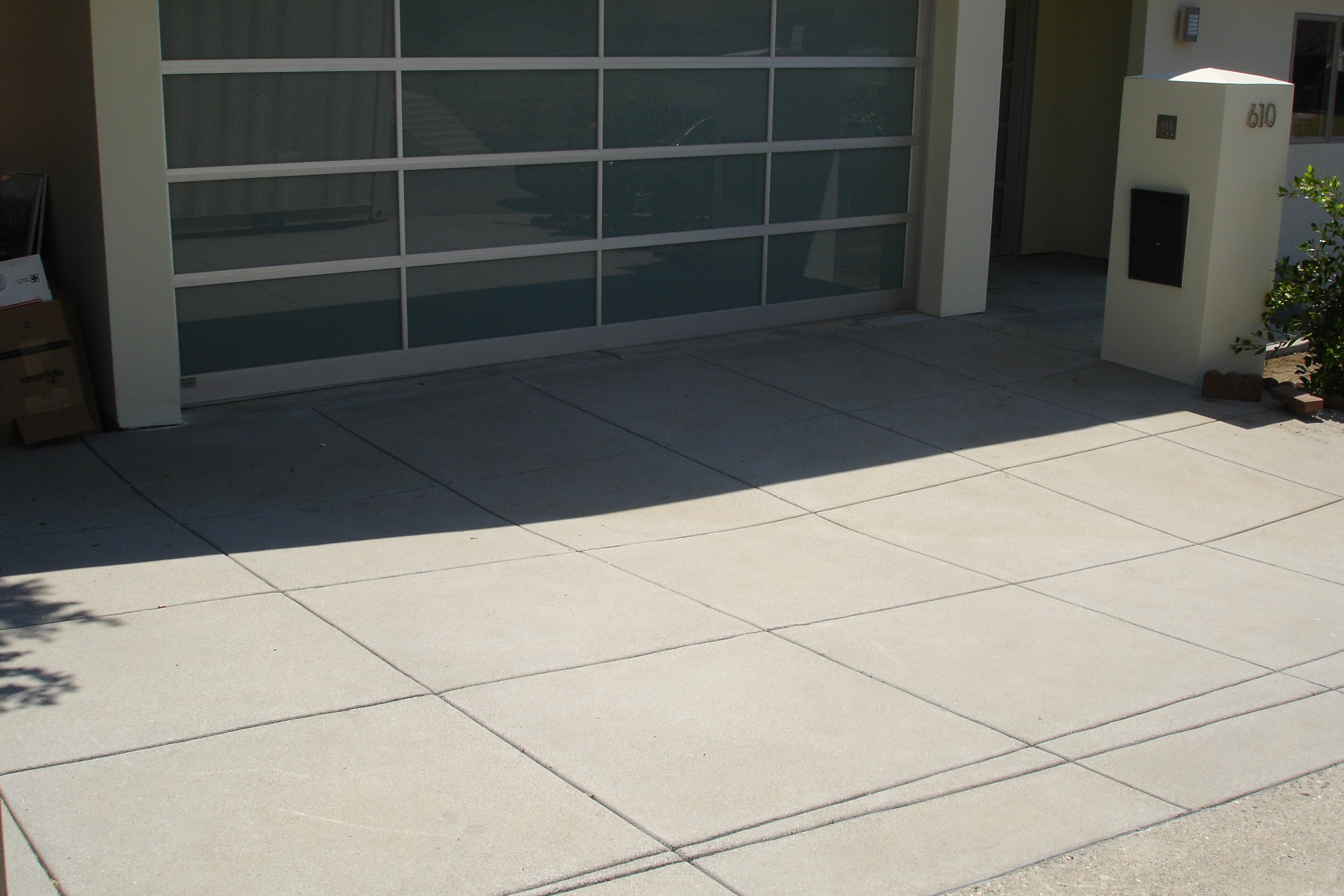 Sand finish concrete driveway with grid score lines at modern home with glass garage door in Pacific Palisades, Los Angeles by Concrete Etc., Inc.