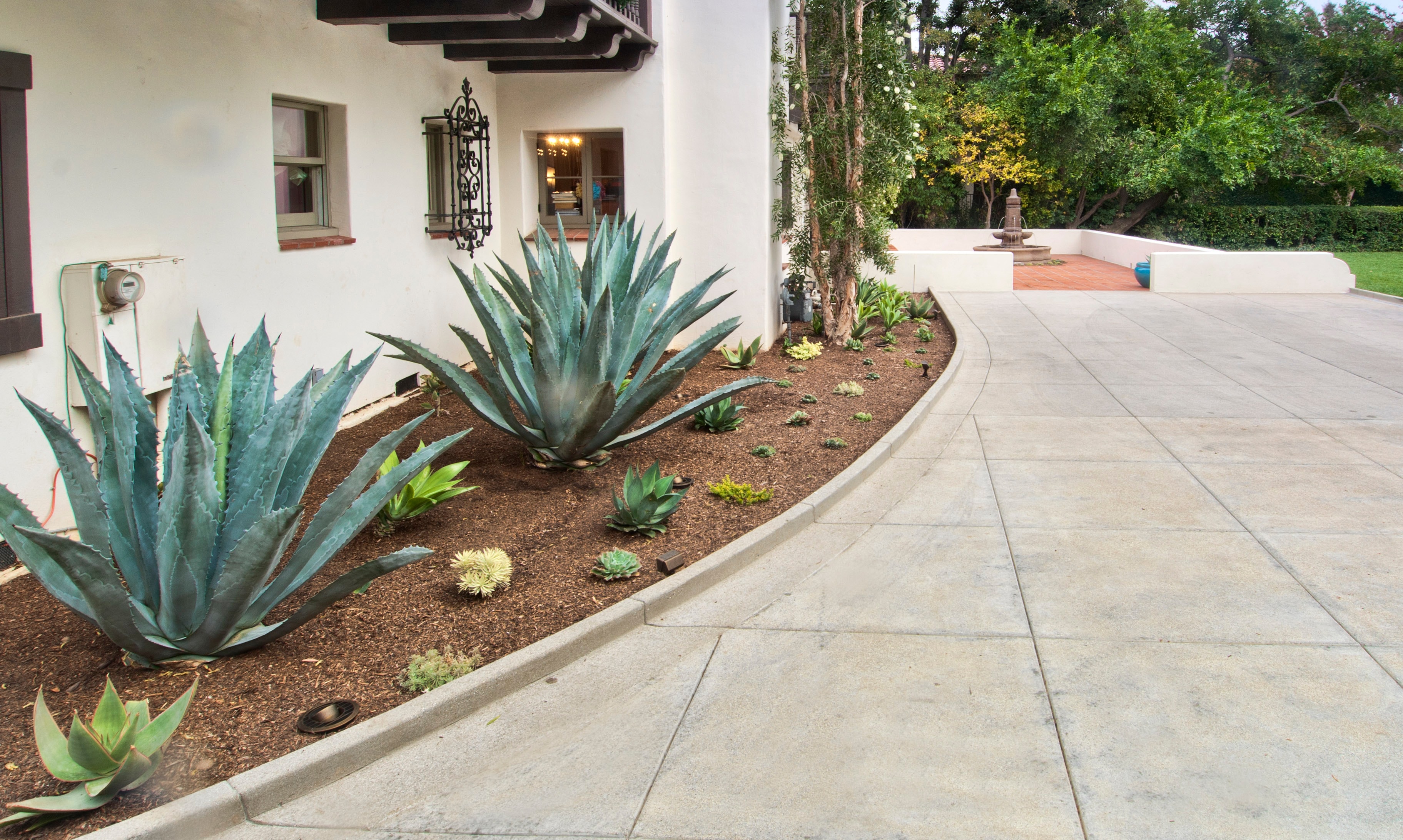 Curved sand finish concrete driveway with decorative score lines alongside desert landscaping with agave plants at a Spanish-style home in Pasadena by Concrete Etc., Inc.