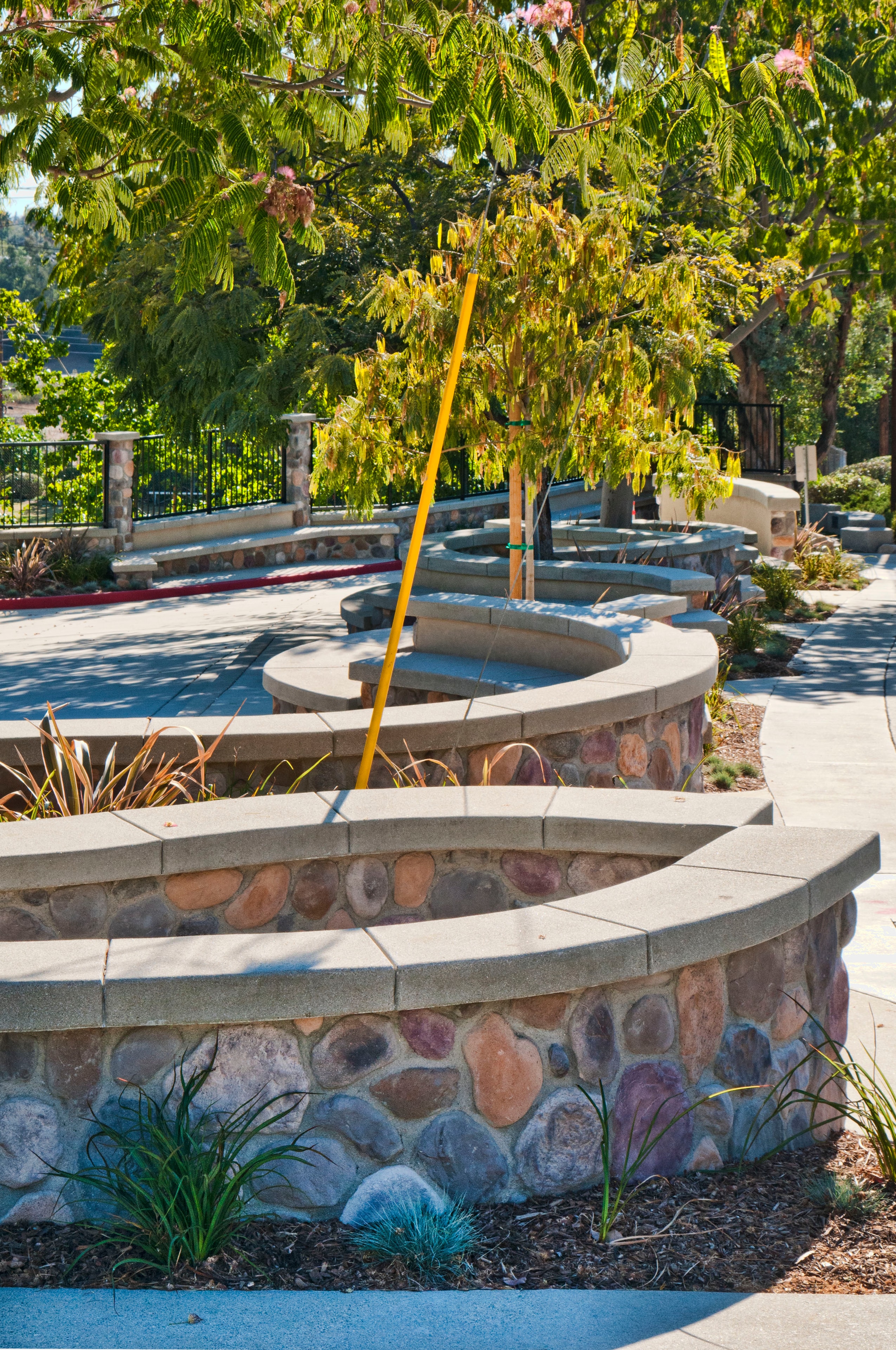 Curved stone veneer seating walls with poured-in-place concrete caps and sand finish concrete walkways at a school remodel in Pasadena by Concrete Etc., Inc.